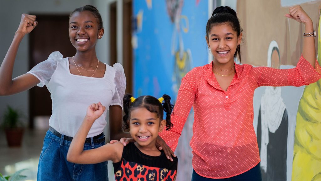 Three girls raise their arms smiling.